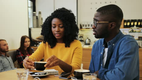 Hombre-Y-Mujer-Afroamericanos-Hablando-Y-Bebiendo-Café-Sentados-En-Una-Mesa-En-Un-Café