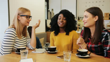 African-american-and-caucasian-women-friends-gossiping-and-laughing-sitting-at-a-table-in-a-cafe