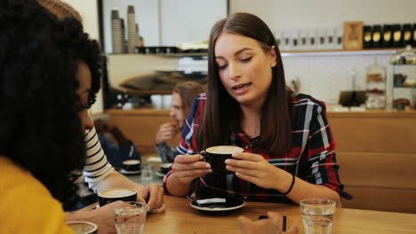 Close-up-view-of-african-american-and-caucasian-women-friends-talking-and-drinking-coffee-sitting-at-a-table-in-a-cafe