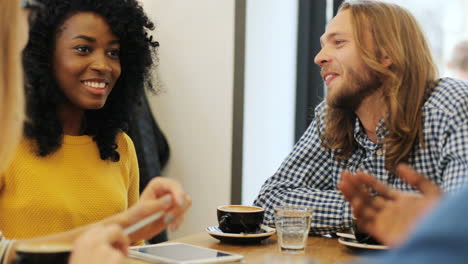Close-up-view-of-multiethnic-group-of-friends-laughing-and-drinking-coffee-sitting-at-a-table-in-a-cafe