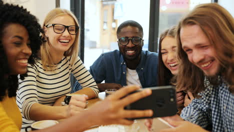 Close-up-view-of-multiethnic-group-of-friends-talking-and-watching-a-video-on-a-smartphone-sitting-at-a-table-in-a-cafe