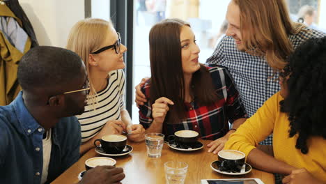 Close-up-view-of-multiethnic-group-of-friends-talking-and-laughing-sitting-at-a-table-in-a-cafe