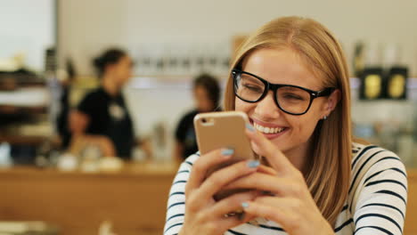Close-up-view-of-caucasian-blonde-woman-in-glasses-texting-on-the-phone-sitting-at-a-table-in-a-cafe
