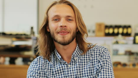 Close-up-view-of-caucasian-blond-man-with-long-hair-smiling-at-camera-sitting-at-a-table-in-a-cafe