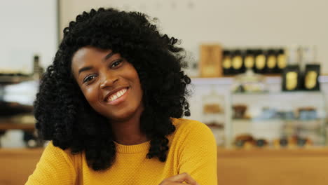 Close-up-view-of-african-american-woman-with-curly-hair-smiling-at-camera-sitting-at-a-table-in-a-cafe