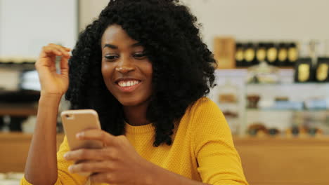 Close-up-view-of-african-american-woman-with-curly-hair-texting-on-the-phone-sitting-at-a-table-in-a-cafe