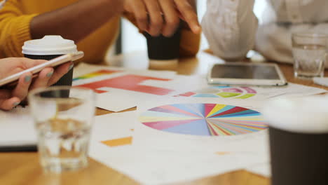 Close-up-view-of-hands-of-multiethnic-people-pointing-graphics-on-a-table-in-a-cafe