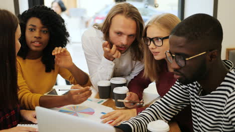 Close-up-view-of-multiethnic-coworkers-viewing-graphics-and-talking-sitting-at-a-table-in-a-cafe