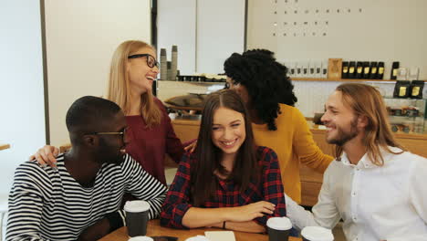 Multiethnic-group-of-friends-smiling-and-looking-at-camera-sitting-at-a-table-in-a-cafe