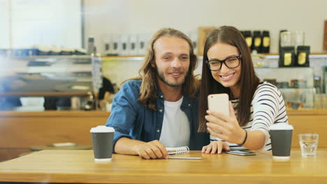 Kaukasische-Freunde,-Die-Einen-Videoanruf-Mit-Dem-Smartphone-Machen,-Sitzen-An-Einem-Tisch-In-Einem-Café