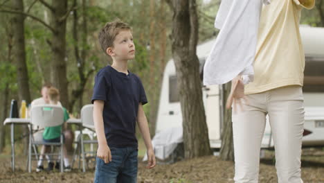Little-boy-helping-her-mother-to-hang-out-washing-clothes-on-clothesline-at-the-camping-in-the-forest