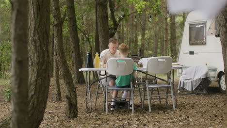 Vater-Und-Sohn-Spielen-Schach,-Während-Sie-Auf-Dem-Campingplatz-Im-Wald-Am-Tisch-Sitzen