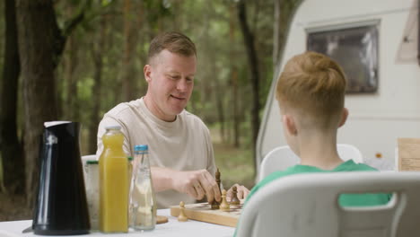 Father-and-son-playing-chess-while-sitting-at-table-at-the-camping-in-the-forest