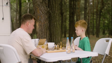 Father-and-son-playing-chess-at-the-camping-in-the-forest