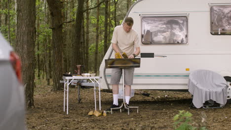 Man-collecting-wood-and-putting-it-in-a-grill-at-the-camping-in-the-forest