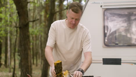 Caucasian-man-putting-wood-in-a-grill-at-the-camping-in-the-forest