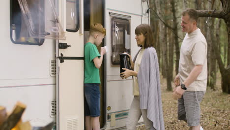 Happy-mother-pouring-tea-from-kettle-into-her-son's-cup-while-standing-by-the-campervan-in-the-forest