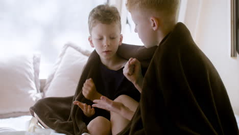 Two-little-brothers-with-blanket-on-their-shoulders-sitting-on-bed-in-a-campervan-and-playing-rock-scissors-paper