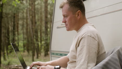 Concentrated-man-working-on-laptop-computer-at-the-camping-in-the-forest