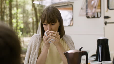 Smiling-woman-drinking-coffee-while-having-breakfast-with-her-family-at-the-camping-in-the-forest
