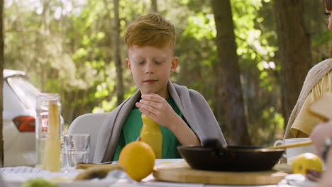 Little-boy-having-breakfast-with-his-family-at-the-camping-in-the-forest