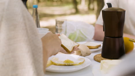 Close-up-of-an-unrecognizable-woman-spreading-butter-on-toast-while-having-breakfast-outdoors