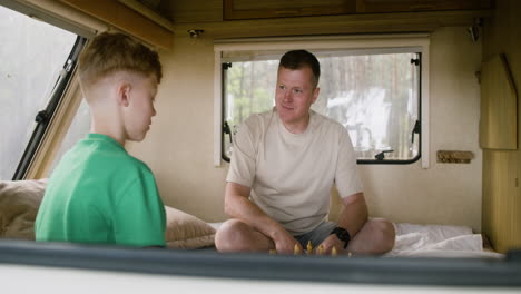 Father-and-son-playing-chess-sitting-on-the-campervan-bed