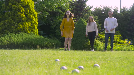 Distant-view-of-two-caucasian-young-women-and-a-man-playing-petanque-in-the-park-on-a-sunny-day