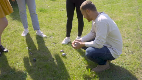 Side-view-of-a-caucasian-young-man-calculating-distance-between-petanque-balls-in-the-park