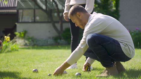 Side-view-of-a-caucasian-young-man-calculating-distance-between-petanque-balls-in-the-park