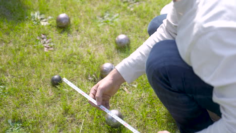 Close-up-view-of-a-caucasian-young-man-calculating-distance-between-petanque-balls-in-the-park