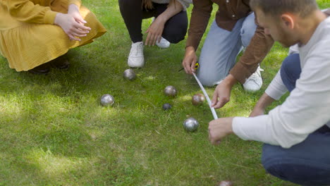 Close-up-view-of-a-group-of-men-and-women-friends-calculating-distance-between-petanque-balls-in-the-park