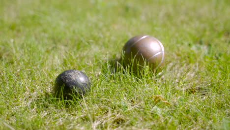 Close-up-view-of-two-metal-petanque-balls-on-the-grass,-then-another-ball-crash-with-one-of-them