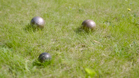 Close-up-view-of-three-metal-petanque-balls-on-the-grass,-then-the-player-throw-another-ball-nearby