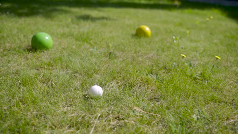 Close-up-view-of-three-colorful-petanque-balls-on-the-grass,-then-the-player-throw-another-ball-nearby