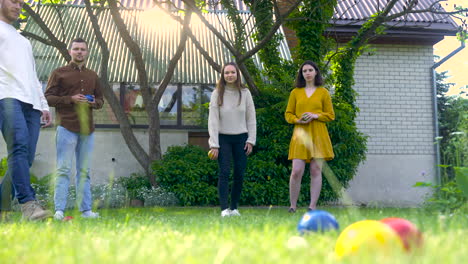 Caucasian-young-woman-throwing-a-yellow-petanque-ball-in-the-park-on-a-sunny-day-while-her-friends-wait-their-turns