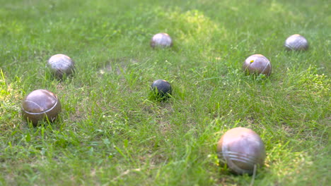 Camera-zooming-on-black-metal-metal-petanque-ball-surrounded-by-other-balls-on-the-grass-in-the-park