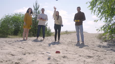 Front-view-of-caucasian-group-of-women-and-men-friends-playing-petanque-on-the-beach