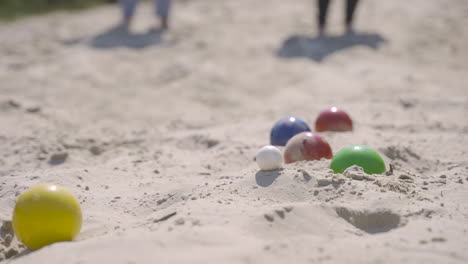 Close-up-view-of-colorful-petanque-balls-on-the-sand-on-the-beach,-then-a-player-throws-another-ball-nearby