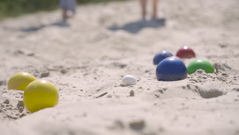 Nahaufnahme-Von-Bunten-Pétanque-Kugeln-Im-Sand-Am-Strand,-Dann-Wirft-Ein-Spieler-Einen-Anderen-Ball-In-Der-Nähe