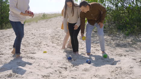 Group-of-women-and-men-friends-picking-up-petanque-balls-from-the-sand-on-the-beach-on-a-sunny-day