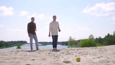 Two-caucasian-young-man-friends-playing-petanque-on-the-beach-on-a-sunny-day
