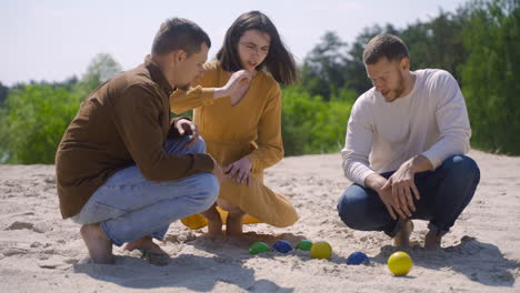 Group-of-caucasian-young-friends-calculating-distance-between-petanque-balls-on-the-beach-on-a-sunny-day
