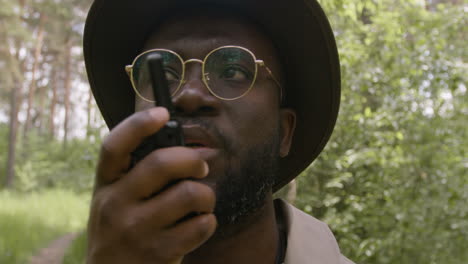 Close-up-view-of-african-american-forest-warden-with-sunglasses-talking-on-walkie-talkie-in-the-woods