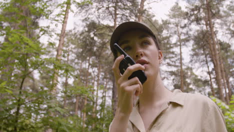 Lower-view-of-caucasian-female-forest-warden-talking-on-walkie-talkie-in-the-woods