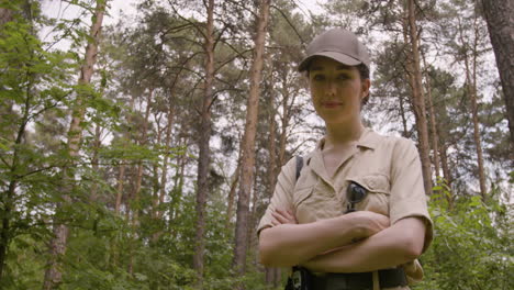 Lower-view-of-caucasian-female-forest-warden-wearing-cap-and-looking-at-camera-with-crossed-arms-in-the-woods