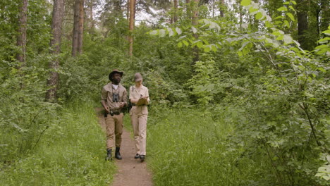 Distant-view-of-caucasian-and-african-american-forest-wardens-taking-notes-and-talking-while-walking-in-the-woods
