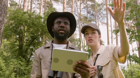 Caucasian-and-african-american-forest-wardens-watching-something-on-the-tablet-and-talking-in-the-woods