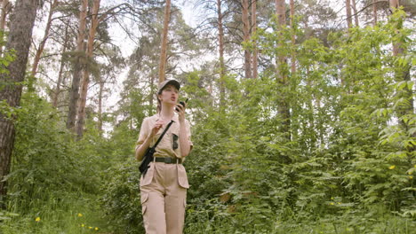 Lower-view-of-caucasian-female-forest-warden-talking-on-walkie-talkie-and-walking-in-the-woods