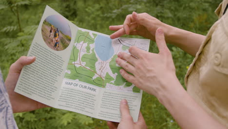 Close-up-view-of-caucasian-forest-warden-hands-pointing-on-the-map-of-a-tourist-in-the-woods